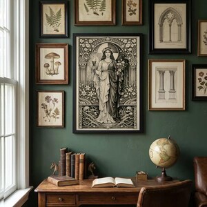 May include: A gallery wall featuring a large central framed print of a figure holding a torch and flowers, surrounded by smaller framed botanical and architectural prints. Below, a wooden desk holds a row of books, an open book, and a globe.