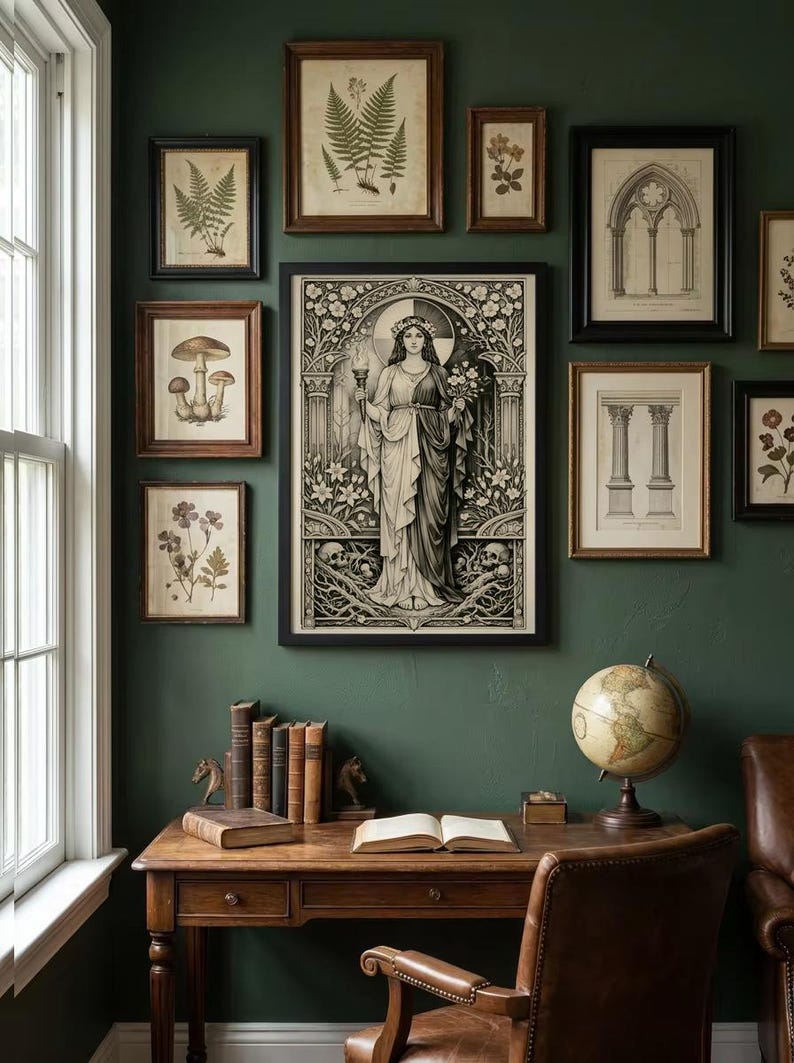 May include: A gallery wall featuring a large central framed print of a figure holding a torch and flowers, surrounded by smaller framed botanical and architectural prints. Below, a wooden desk holds a row of books, an open book, and a globe.