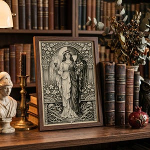 May include: A rectangular framed print featuring a black and white illustration of a central female figure holding a torch and flowers, surrounded by an ornate archway, floral motifs, and skulls at the base, enclosed in a dark brown wooden frame.