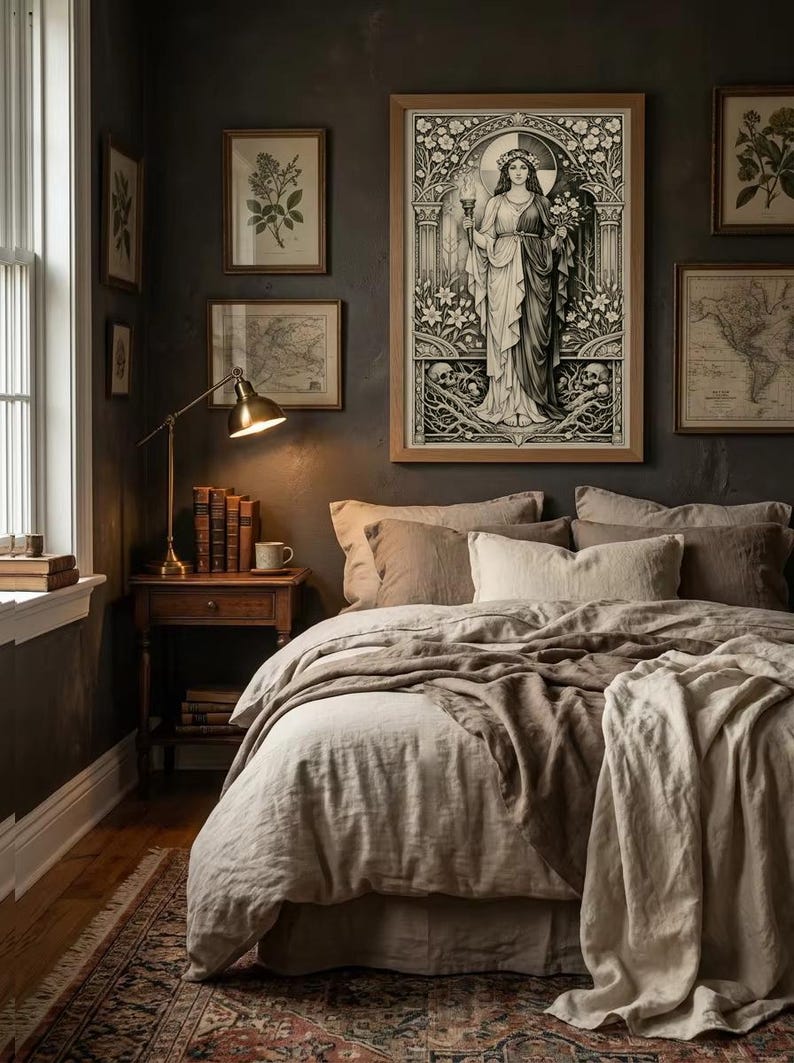 May include: A framed black and white art print depicting a central figure holding a torch and flowers, surrounded by ornate floral borders and skulls. The artwork is displayed on a dark wall above a bed with layered beige and brown bedding.