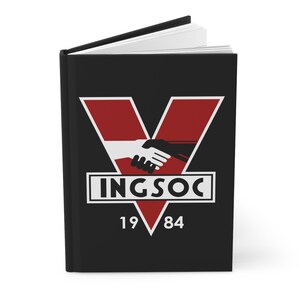May include: Black journal with a red and white graphic of two hands shaking inside a red V-shaped design. The word "INGSOC" is in a white rectangle, with "19" and "84" below. The journal is open, revealing white pages.