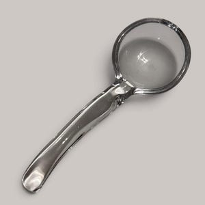 May include: A clear, transparent glass scoop featuring a rounded, deep bowl and a smooth, curved handle. The utensil is constructed from a single piece of molded glass, showcasing a polished, reflective surface throughout its entire structure.