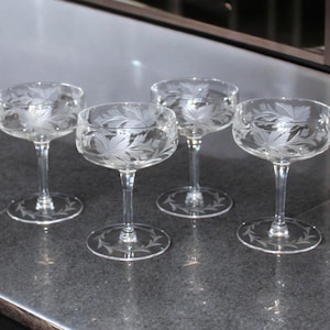 Peut inclure: Quatre coupes à champagne transparentes avec des motifs de feuilles gravées. Les verres ont un bol rond, une tige fine et une base circulaire. Le motif de feuille est répété sur la base de chaque verre.
