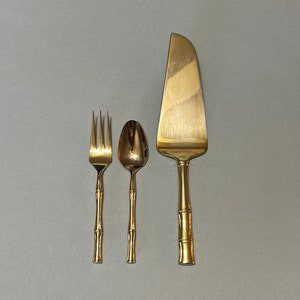 May include: A set of three gold-toned utensils with bamboo-style handles. The set includes a fork, a spoon, and a cake server.
