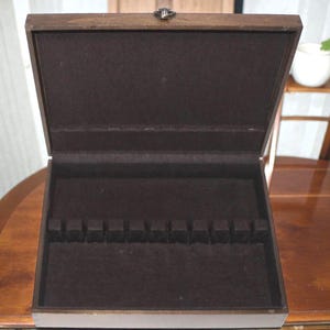 May include: A rectangular wooden storage box with a hinged lid and a dark brown finish. The interior is lined with dark brown fabric and features a row of twelve small, evenly spaced vertical dividers designed for organizing flat items.