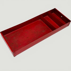 Peut inclure: Un bac à outils en métal rouge, de forme rectangulaire avec plusieurs compartiments. Le bac présente une finition usée, indiquant une utilisation. Les compartiments sont de tailles différentes, pour ranger des outils ou petits objets. Mesure environ 40 cm de long.