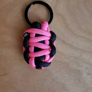 May include: A pink and black paracord keychain with a black metal key ring.