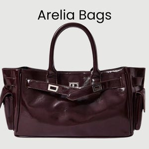 May include: A glossy, dark burgundy handbag with a top handle and side pockets. It features a flap closure with a silver buckle. The text "Arelia Bags" is displayed at the top of the image.