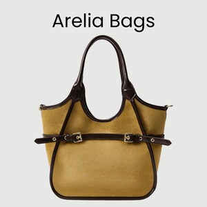 May include: Arelia Bags tote bag. Tan-colored tote bag with dark brown leather trim, handles, and straps. The bag features two buckle closures and a structured design. The brand name "Arelia Bags" is displayed at the top.