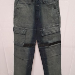 Puede incluir: Pantalones cargo de mezclilla azul con múltiples bolsillos y detalles en negro. Los pantalones tienen un lavado descolorido y un ajuste relajado. El diseño incluye bandas negras alrededor de las rodillas. Un estilo casual para el día a día.