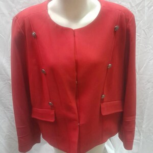 Peut inclure: Un blazer rouge vif avec un col rond et des manches longues. Le blazer est orné de boutons argentés et de deux poches avant. Le vêtement est présenté sur un mannequin.