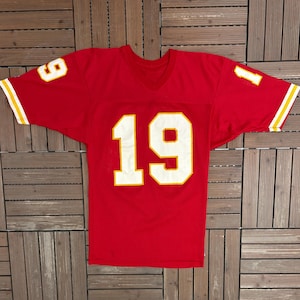 May include: A red football jersey featuring the number 19 in white with a yellow outline on the front. The number 9 is on the left shoulder and the number 1 on the right. Sleeves have yellow and white stripes. A classic sports jersey.