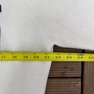 K&ouml;nnte beinhalten: Ein wei&szlig;es Sweatshirt mit dunkelblauem Akzent. Ein gelbes Ma&szlig;band zeigt eine Brustweite von ca. 61 cm. Das Sweatshirt ist aus einem weichen, strukturierten Stoff gefertigt.