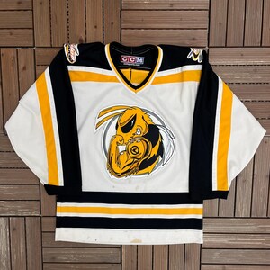 May include: White, black, and yellow hockey jersey with a V-neck collar. The jersey features a large cartoon wasp emblem on the front. The sleeves are black with yellow stripes. The jersey has a CCM tag.