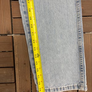 May include: Light blue denim jeans with a frayed hem. A yellow measuring tape shows a length of approximately 31 inches. The jeans are on a wooden surface.