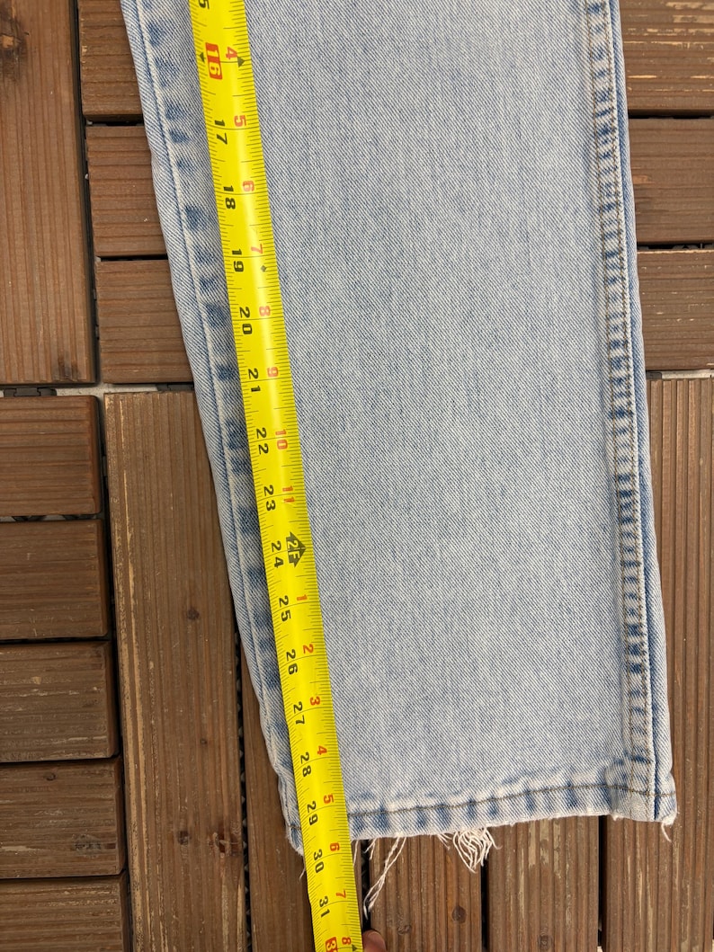 May include: Light blue denim jeans with a frayed hem. A yellow measuring tape shows a length of approximately 31 inches. The jeans are on a wooden surface.