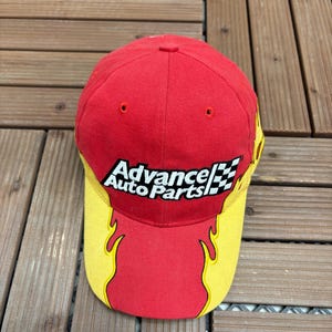 May include: Red baseball cap with a yellow brim and flame design. The cap features the "Advance Auto Parts" logo in white with a checkered flag graphic. A classic, sporty accessory.
