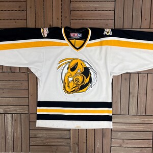 May include: White hockey jersey with black and yellow accents. The jersey features a large cartoon wasp logo on the front, with black sleeves and yellow stripes. The jersey has a V-neck collar and the CCM logo.