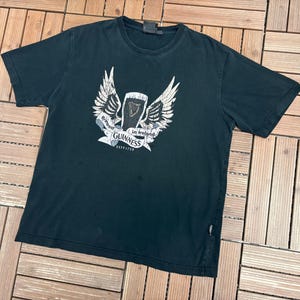 May include: Black t-shirt featuring a white graphic of a pint of Guinness with wings and the text "Brewed in Ireland Guinness ESTD 1759". The shirt is made of a soft material and has a crew neck.