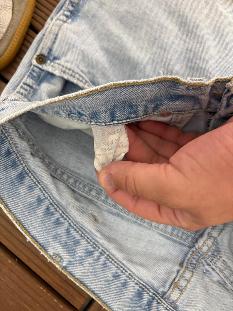 May include: Light blue denim jeans with a faded wash. The jeans have a classic five-pocket design and a button and zipper closure. A tag inside the jeans reads "501 S" and the size "34 x 32".