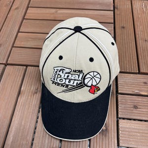 May include: Tan baseball cap with a black brim and the text "2005 NCAA Final Four Mens" embroidered on the front. The cap features a basketball graphic and a red bird logo.