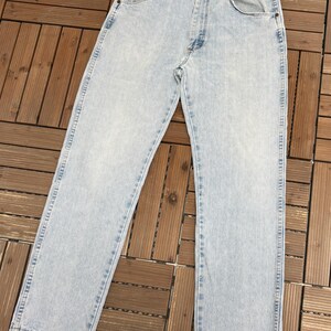 May include: Light blue denim jeans with a classic five-pocket design. The jeans have a straight leg cut and a faded wash, giving them a vintage look. The jeans are made of durable denim material.