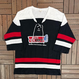 May include: A white ceramic mug with a black handle and the text "But First, Coffee" in a bold, black font. The mug is set against a blurred background, suggesting a cozy setting.