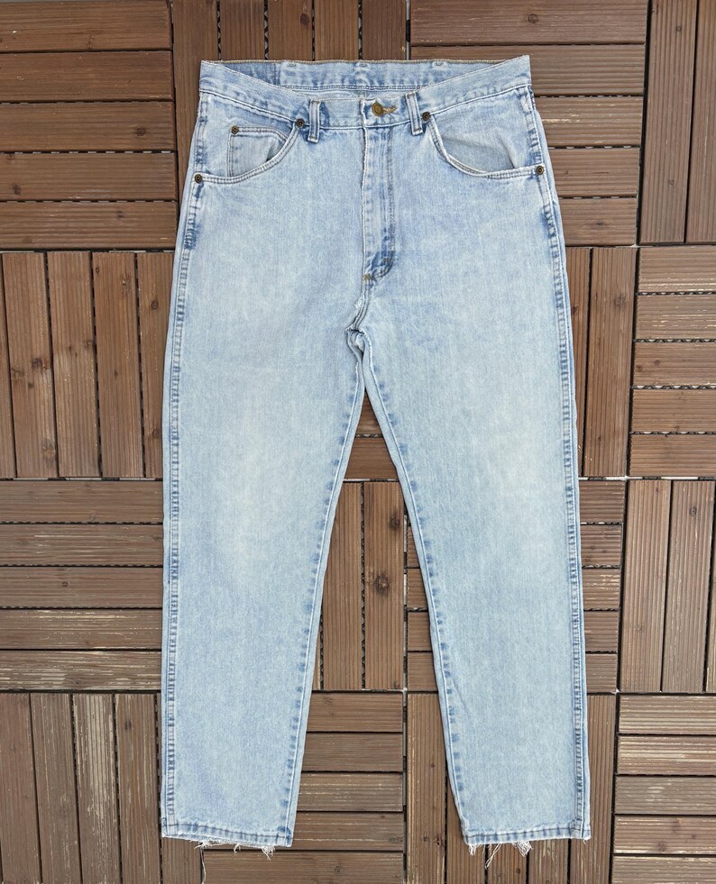 May include: Light blue denim jeans with a classic five-pocket design. The jeans have a straight leg cut and a faded wash, giving them a vintage look. The jeans are made of a durable denim material.