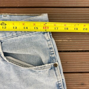 May include: Light blue denim jeans with a pocket and a yellow measuring tape showing a measurement of 16 inches. The jeans are on a wooden surface.
