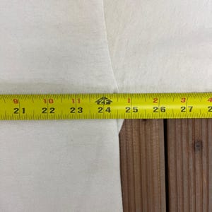 May include: A close-up of white fabric with a yellow measuring tape. The tape shows measurements from 53 cm to 68 cm. The fabric is on a wooden surface.
