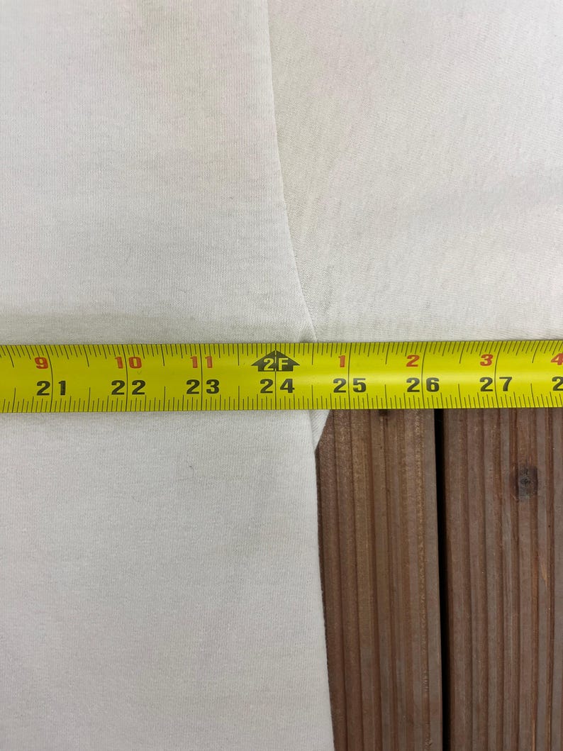 May include: A close-up of white fabric with a yellow measuring tape. The tape shows measurements from 53 cm to 68 cm. The fabric is on a wooden surface.