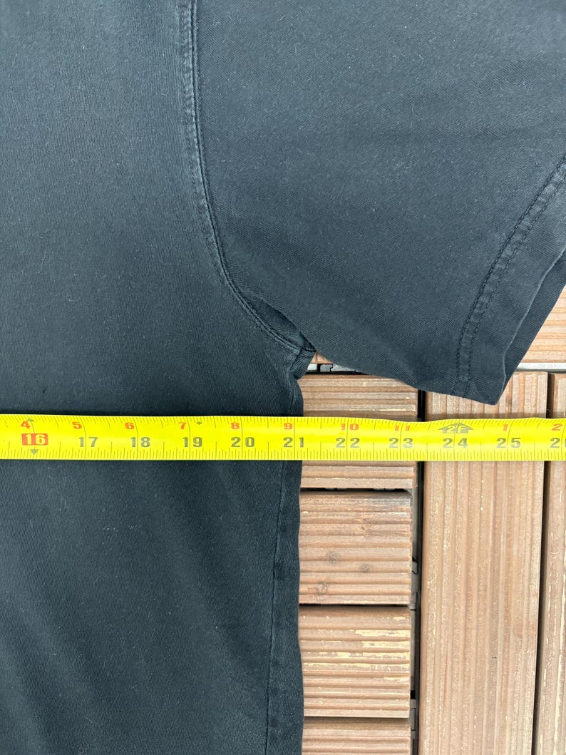 May include: A black t-shirt with a yellow measuring tape laid across the front. The tape measures approximately 9 inches across the chest. The shirt's sleeve is visible on the right side of the image.