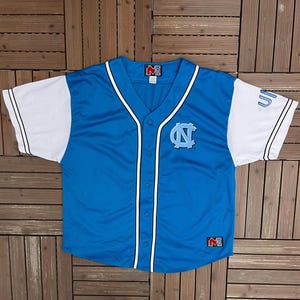 May include: A light blue baseball jersey with white sleeves. The jersey features a button-up front, a V-neck, and the logo of the University of North Carolina on the chest. The sleeves have the word "UN" on them.