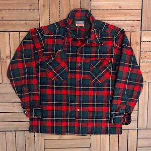May include: A red, green, and yellow plaid flannel shirt with two chest pockets. The long-sleeved shirt has a button-down front and a collar. The shirt is made of a soft, warm material.