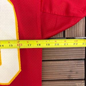 May include: Red mesh jersey with a white and yellow number. A yellow measuring tape shows the jersey is approximately 40.6 cm wide. The jersey is on a wooden surface.