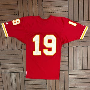 May include: A red Champion jersey featuring the number 19 in white with a gold outline on the front. The sleeves display the numbers 1 and 9 in white with a gold outline. The jersey has gold and white stripes on the sleeves.