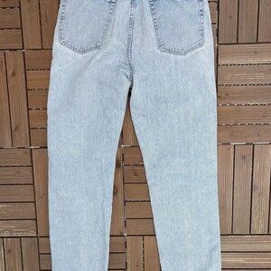 May include: Light blue denim jeans with a classic five-pocket design. The jeans have a faded wash and a straight leg fit. The back pockets are visible, and the Wrangler brand patch is at the waistband.