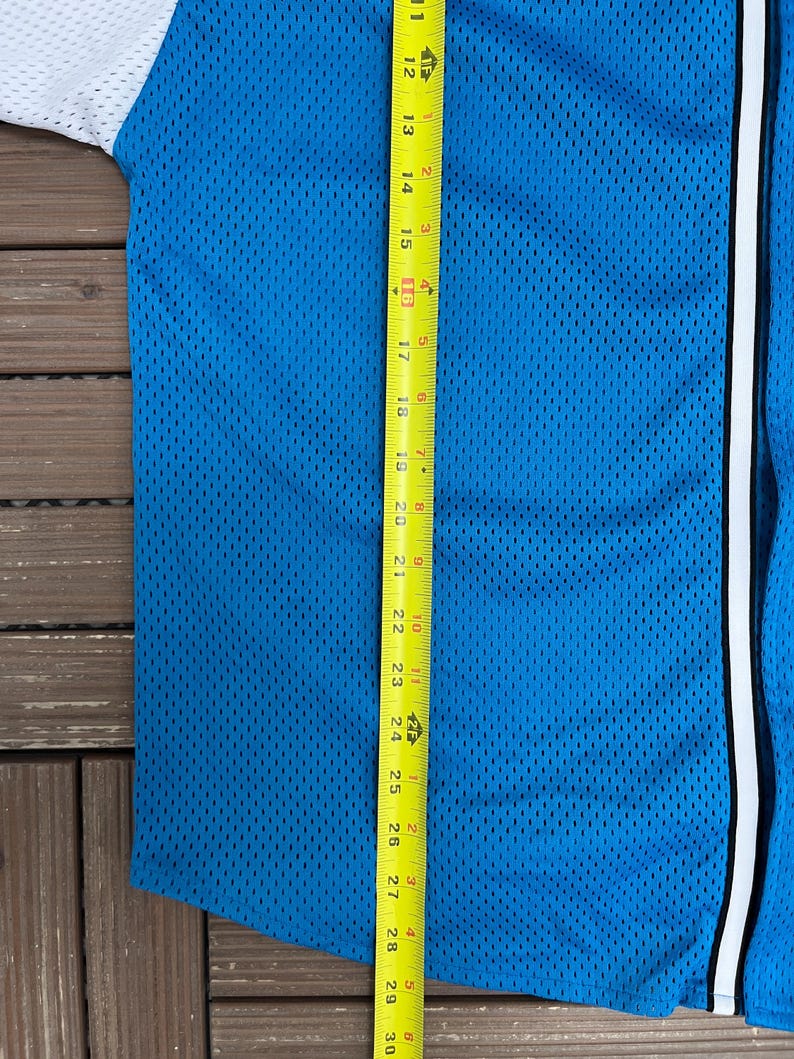 May include: A blue mesh baseball jersey with white sleeves and a white stripe down the front. A yellow tape measure shows the length of the jersey, measuring approximately 30 inches.