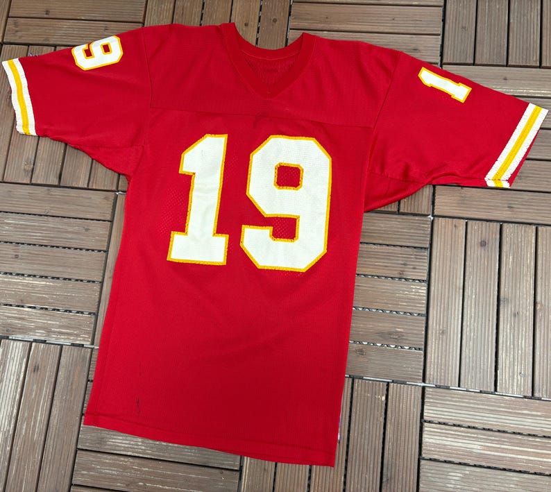 May include: A red football jersey with the number 19 in large white block letters outlined in yellow on the front. The number 1 is visible on the left sleeve and the number 9 on the right sleeve. The sleeves have yellow and white stripes.