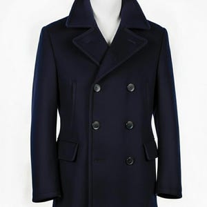 Puede incluir: Un abrigo tipo pea coat azul marino de doble botonadura con cuello ancho y dos filas de botones negros. El abrigo tiene dos bolsillos delanteros y se exhibe en un maniquí blanco. Prenda de abrigo clásica.