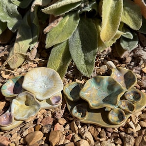 Puede incluir: Dos platos de cerámica con un diseño único. Uno es un grupo de tres platos pequeños, y el otro es un conjunto de cuatro platos pequeños sobre una base rectangular. Los platos tienen una mezcla de colores, incluyendo blanco, amarillo y azul.