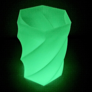 Puede incluir: Un jarrón geométrico verde brillante con un diseño retorcido. El jarrón tiene una forma única con una abertura ancha y una superficie texturizada. El color verde brillante contrasta con el fondo negro, resaltando la forma del jarrón.