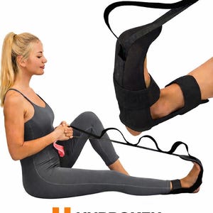 May include: A black stretching strap with multiple loops, used for flexibility exercises. The strap is being used by a person wearing a grey jumpsuit. The word "UNBROKEN" is printed on the bottom of the image.