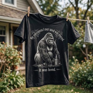May include: A black short-sleeve t-shirt featuring a graphic of a gorilla sitting with a bottle and a cigarette. The text reads, "No substance I ever used was abused. It was loved." The design is rendered in shades of gray and white.