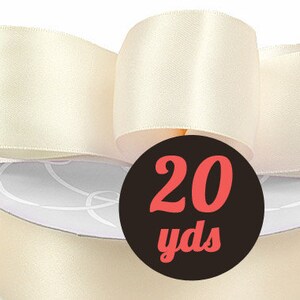 May include: A roll of 20 yards of ivory satin ribbon. The ribbon is wrapped around a spool and tied in a bow.