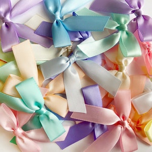 May include: A collection of pastel-colored satin ribbon bows. The bows are arranged in a random pattern and are all tied in a simple knot. The colors of the bows include light pink, light blue, light green, light yellow, and lavender.