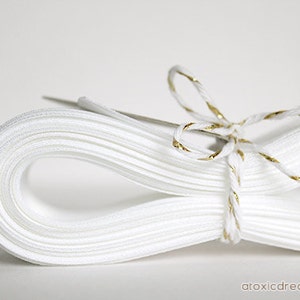 May include: A white satin ribbon tied with a gold and white twine bow. The ribbon is folded and stacked neatly.