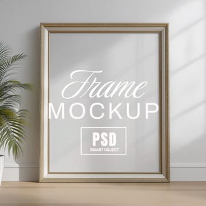 May include: A rectangular frame mockup with a gold-colored trim. The text "Frame MOCKUP" is displayed in a cursive font, with "PSD SMART OBJECT" in a box below. The frame is leaning against a white wall.