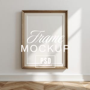 Puede incluir: Una maqueta de marco rectangular con un borde dorado, colgada en una pared blanca. El marco tiene un interior blanco y el texto "Frame MOCKUP PSD SMART OBJECT" está superpuesto. La pared tiene una sombra y está sobre un suelo de madera.