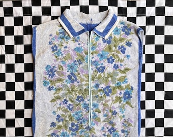May include: A sleeveless, zip-up shirt with a blue and white floral pattern. The shirt has a blue collar and trim.
